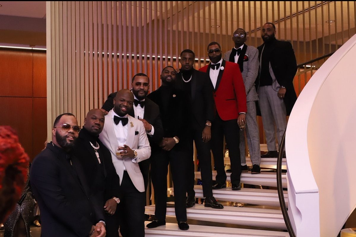 A group of men in formal black tie attire posing on a white staircase.