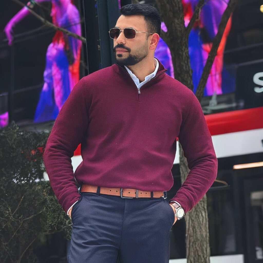Man in a maroon quarter-zip sweater and navy trousers standing outdoors.