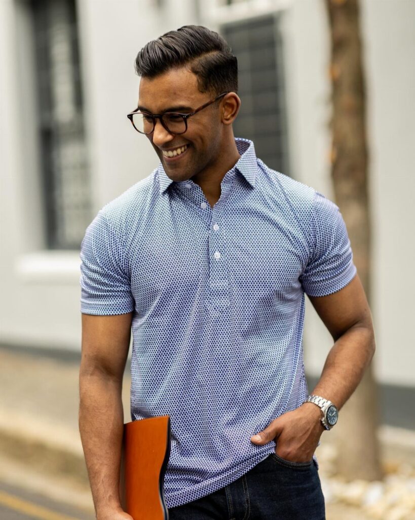 A smiling man in a blue patterned polo shirt and glasses walking outdoors.