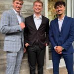 Three young men smiling while wearing stylish suits in light blue plaid, dark brown, and navy blue.