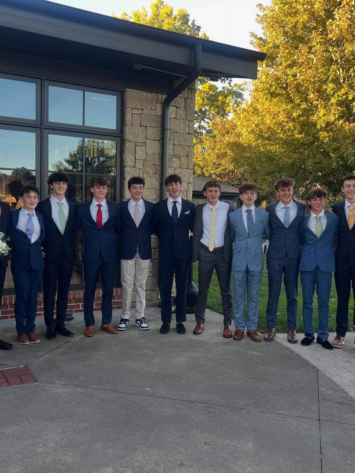 Teenage boys posing in a row wearing various formal suits and ties outdoors.