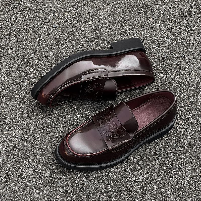 Dark burgundy patent leather loafers resting on a textured grey asphalt ground.