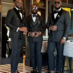 Three men posing in elegant black velvet lapel tuxedos and bow ties in a lounge.
