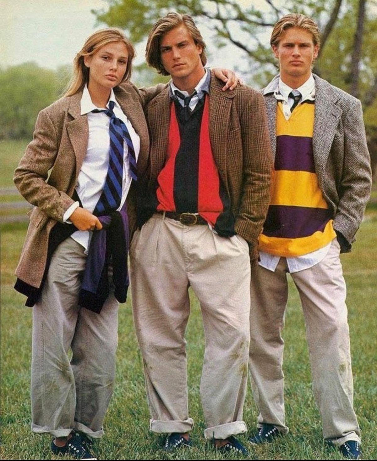 Three young adults posing in classic preppy clothing including blazers, sweaters, and khaki trousers outdoors.