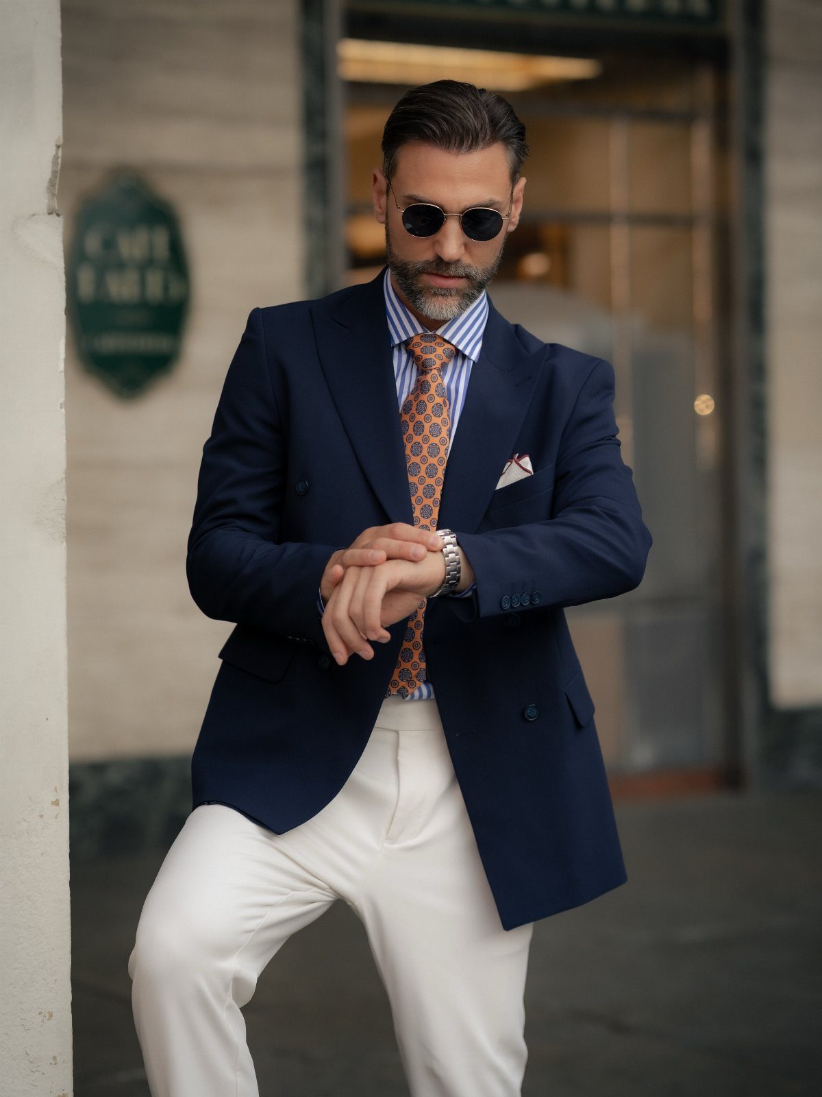 Man in a navy blazer, striped shirt, and orange patterned tie adjusting his watch.