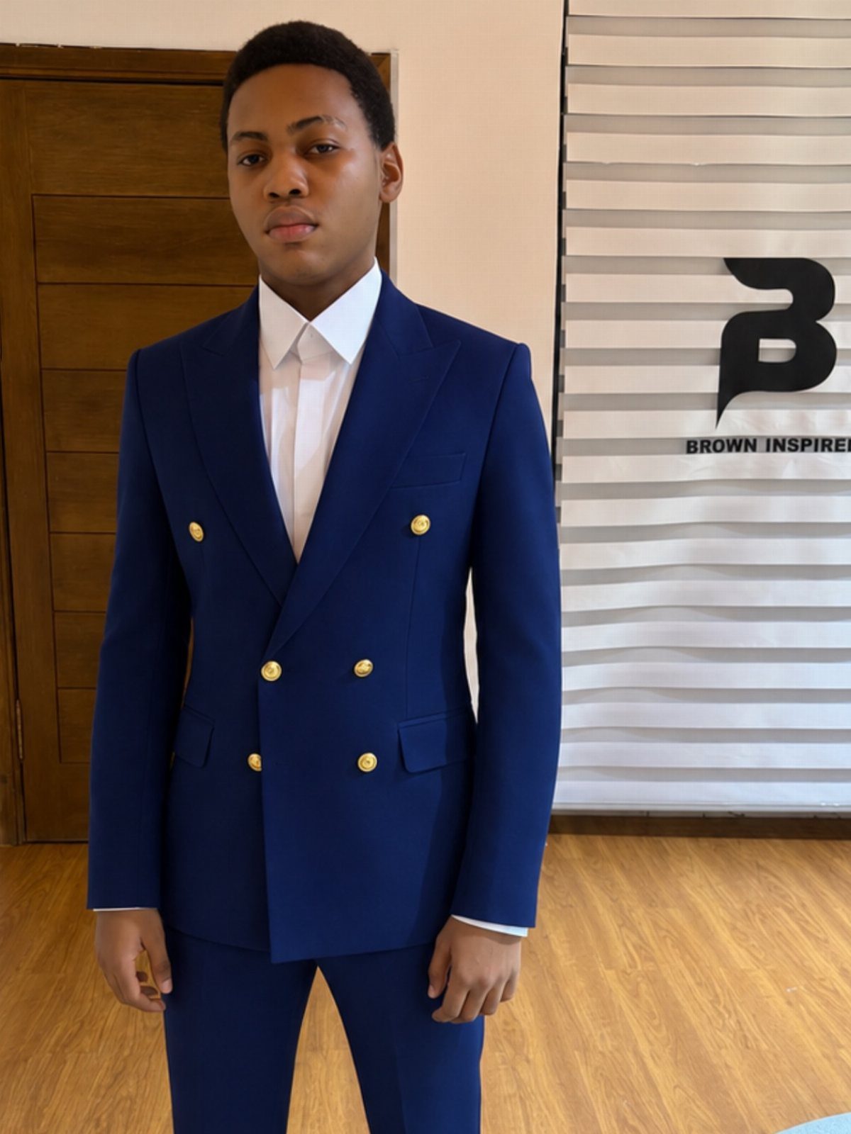 Young man posing in a vibrant blue double-breasted suit with gold buttons and white shirt.