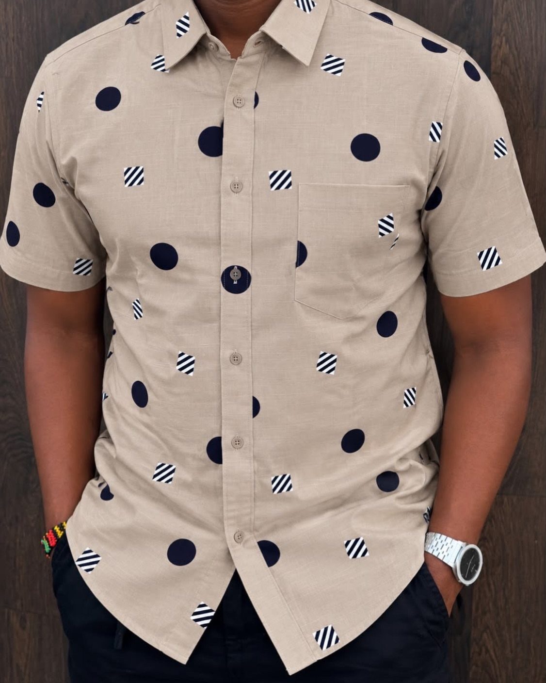 Man wearing a beige short-sleeved button-down shirt with navy blue polka dot patterns.