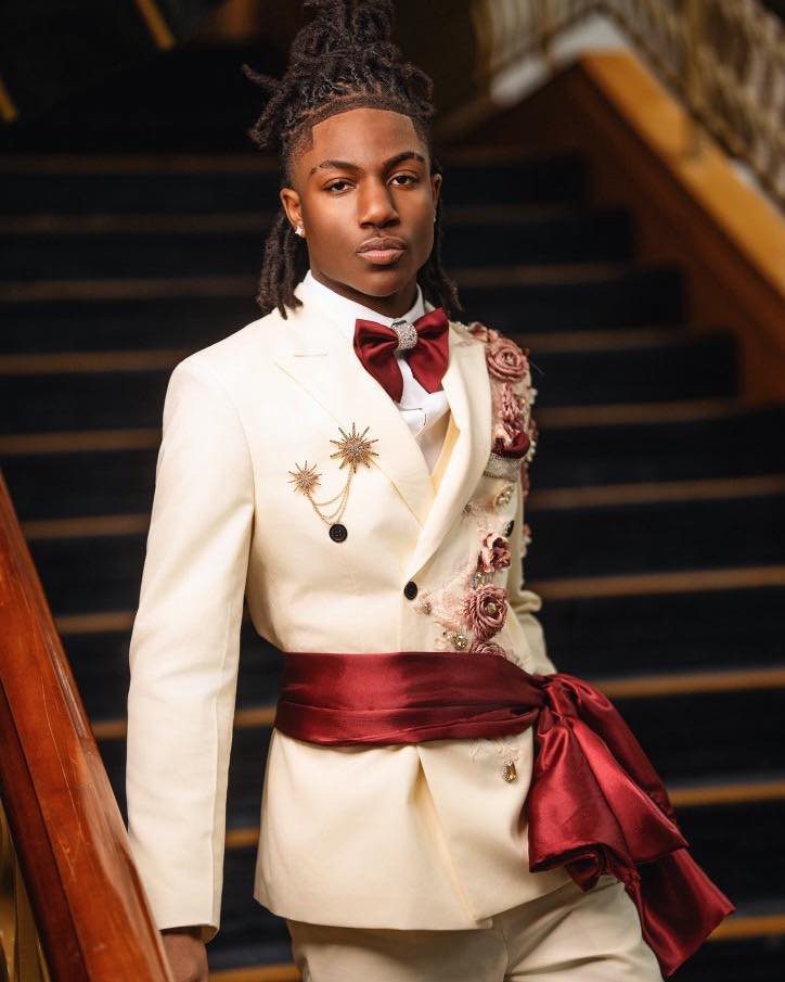 Young man in a cream suit with red floral accents and a large red sash posing on stairs.