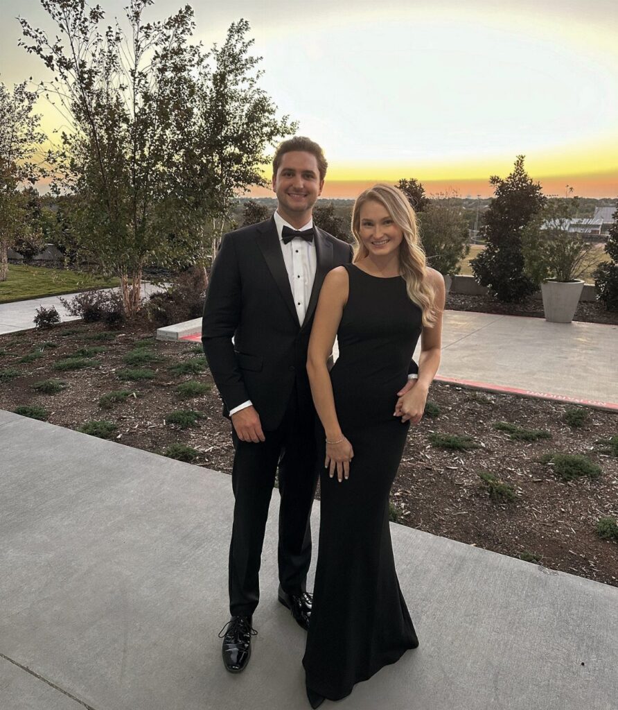 A man in a black tuxedo and a woman in a black floor-length gown posing outdoors.