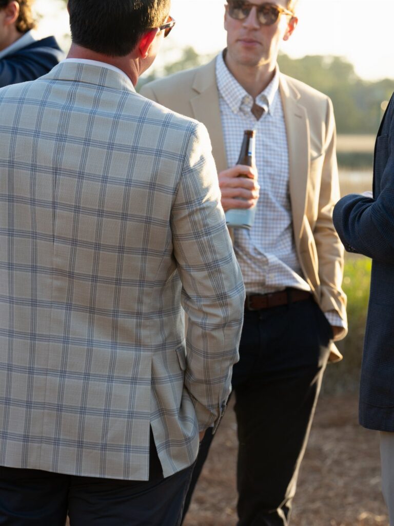 Two men in stylish blazers talking outdoors during a sunny afternoon.