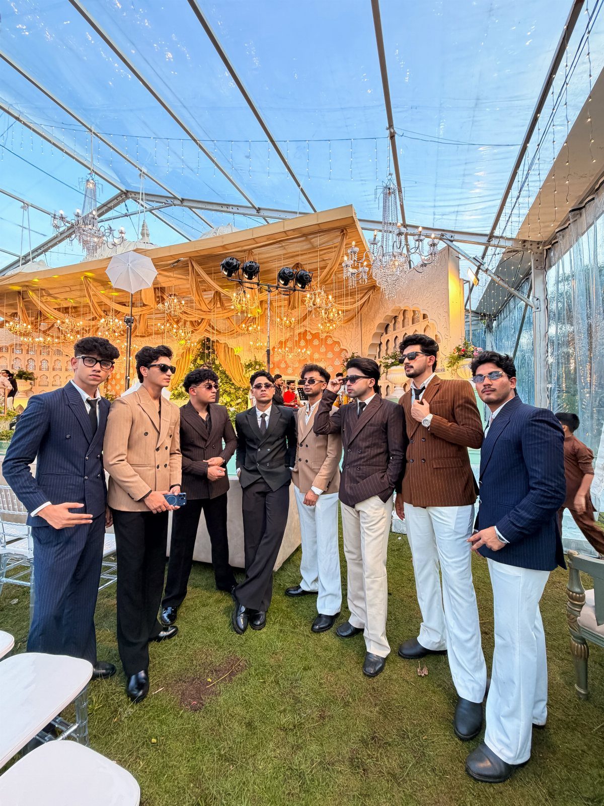 A group of men posing in various formal suits and blazers under a clear canopy.